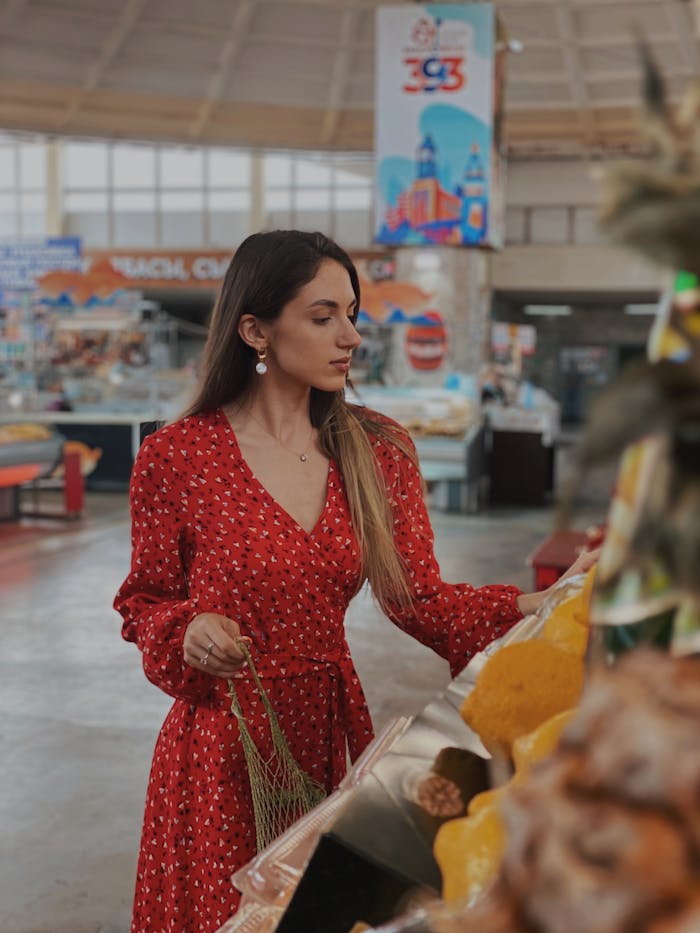 Servicios A stylish woman in a red dress shops for produce in an indoor market setting.